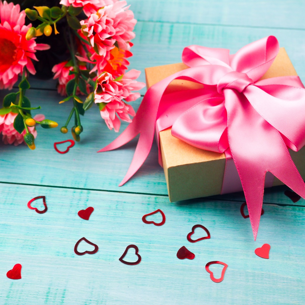 Подарок с розовым бантом на голубом столе с букетом