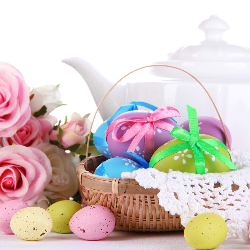 Корзина с пасхальными яйцами на столе с букетом роз и белым чайником