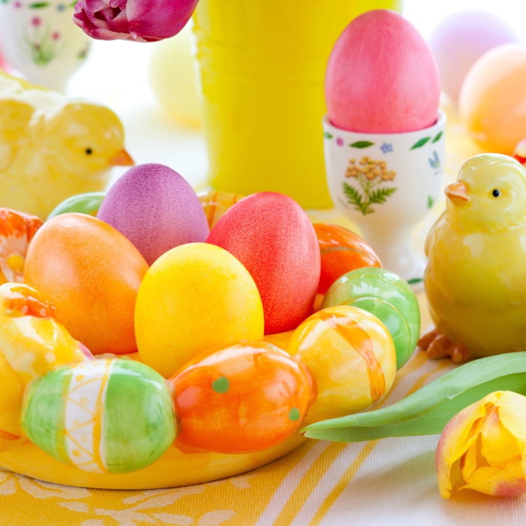 Разноцветные яйца с фигурками на столе с тюльпанами к Пасхе