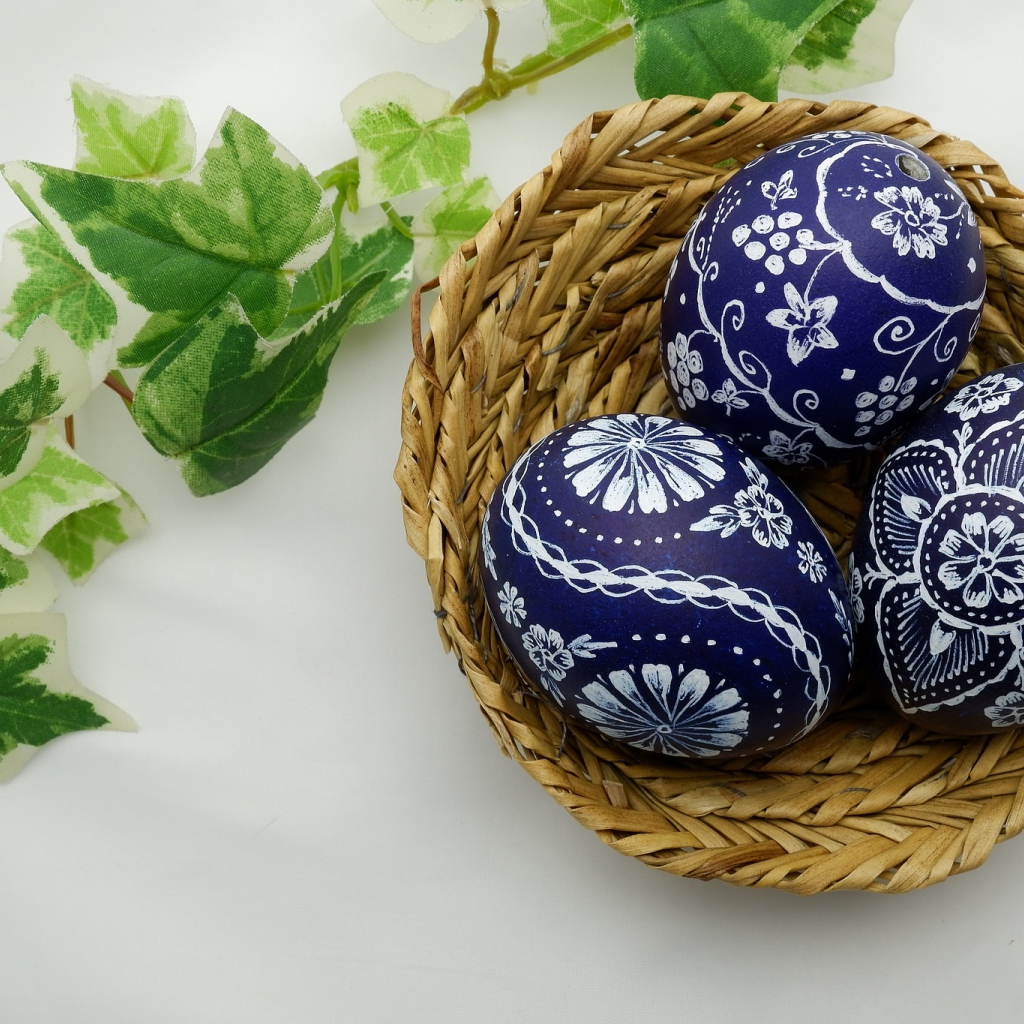 Three painted eggs in a basket on a table with a branch