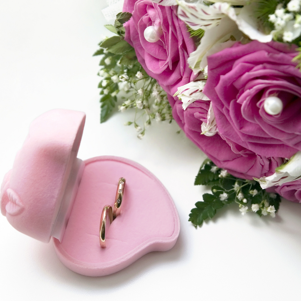 Два обручальных кольца в коробочке на белом фоне с букетом роз