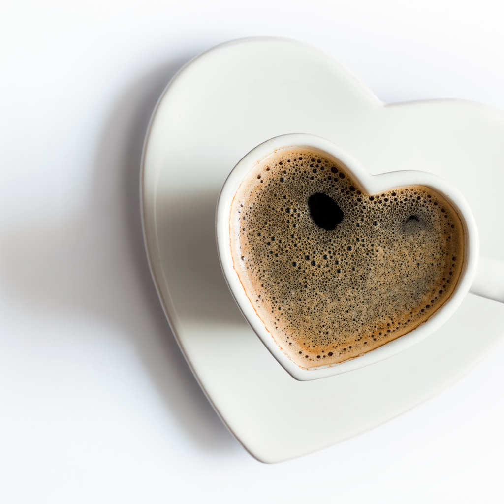 Красивая белая чашка в форме сердца с кофе на белом фоне