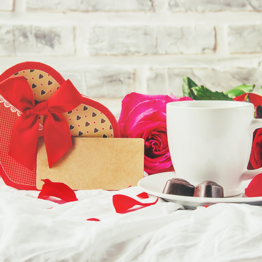 Коробка с подарком на столе с чашкой кофе и красными розами 