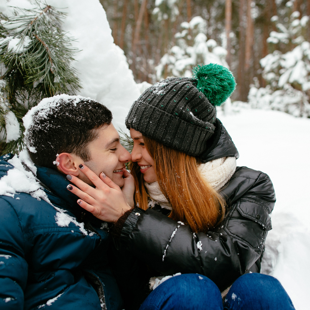 Влюбленная пара сидит под заснеженной еловой веткой зимой