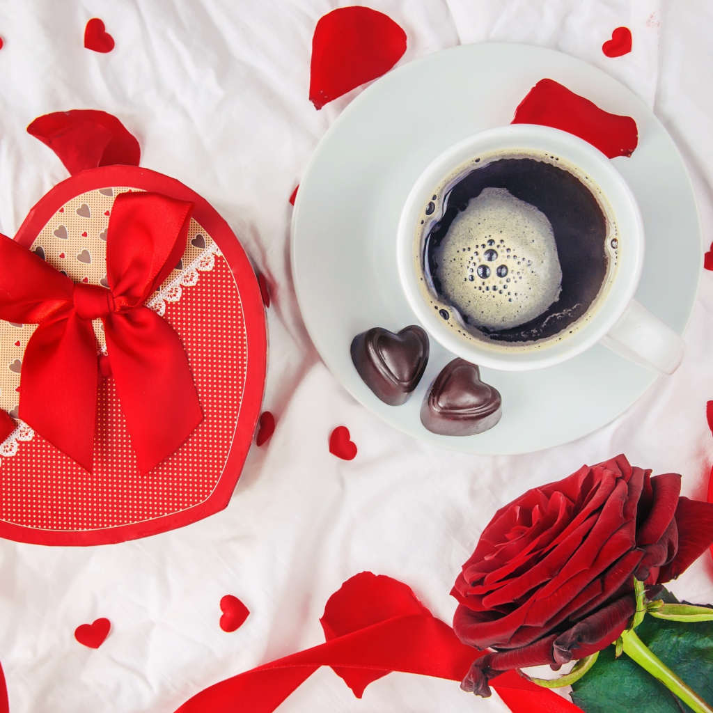 Кружка с кофе и шоколадными конфетами на столе с подарком и красной розой 