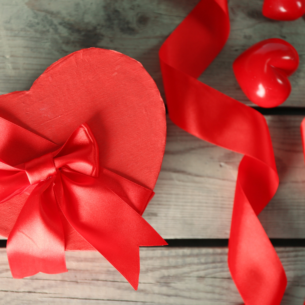 Красная коробка в форме сердца на деревянном столе с красными лентами