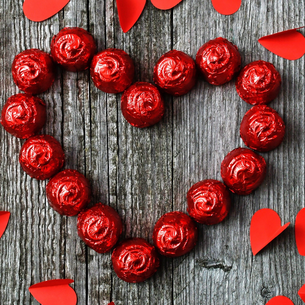 Красное сердце из конфет на деревянном фоне с бумажными сердечками