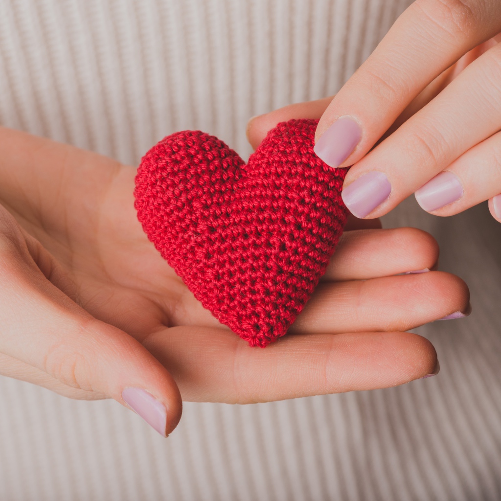 Красное вязаное сердце в руках у девушки