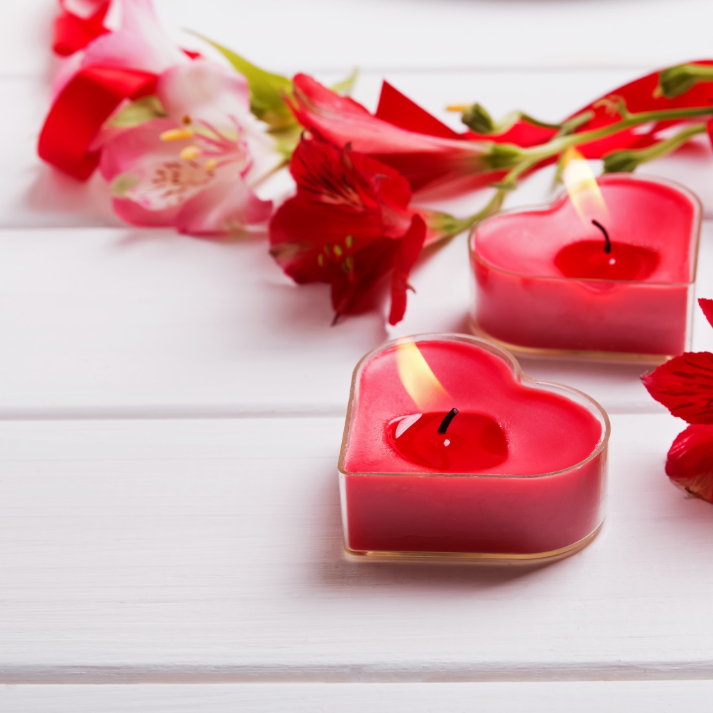 Two red heart-shaped candles on a table with alstroemeria flowers