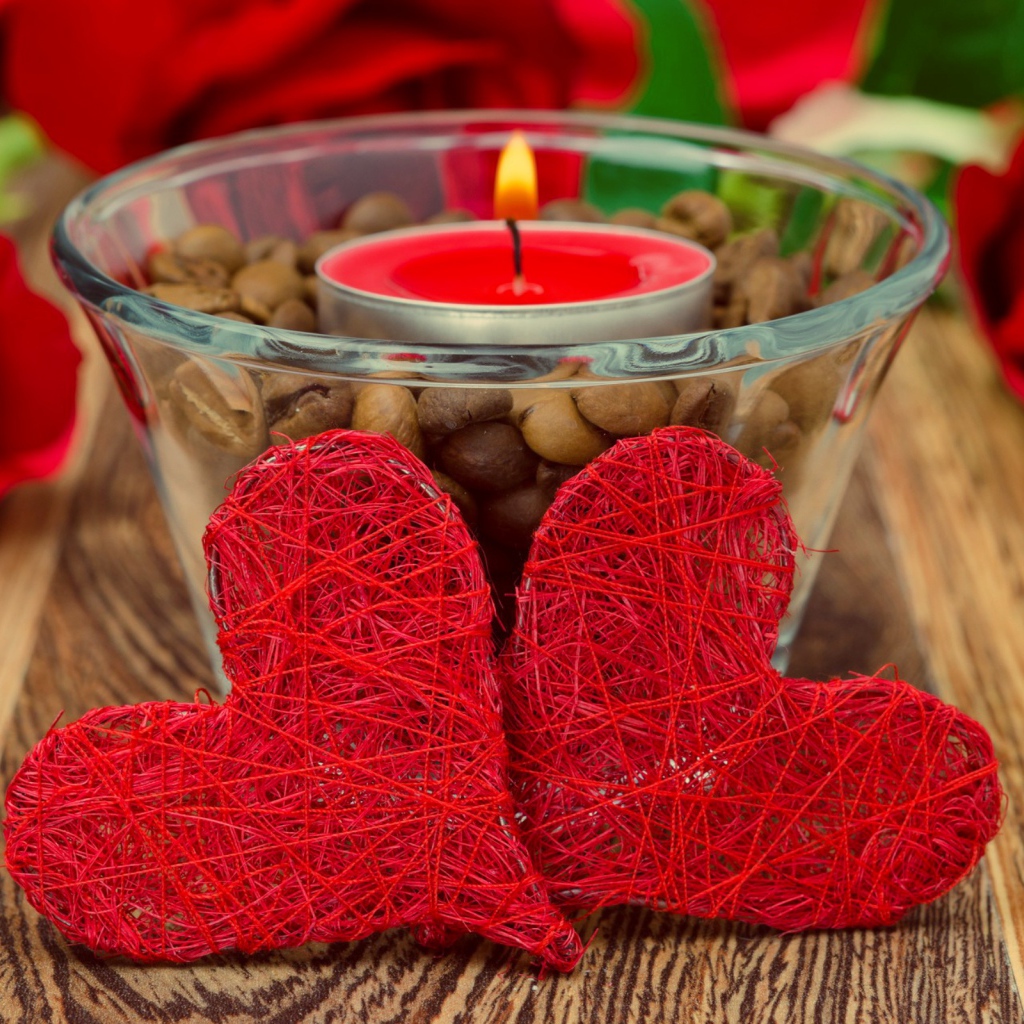 Two red wicker hearts on a table with a burning candle