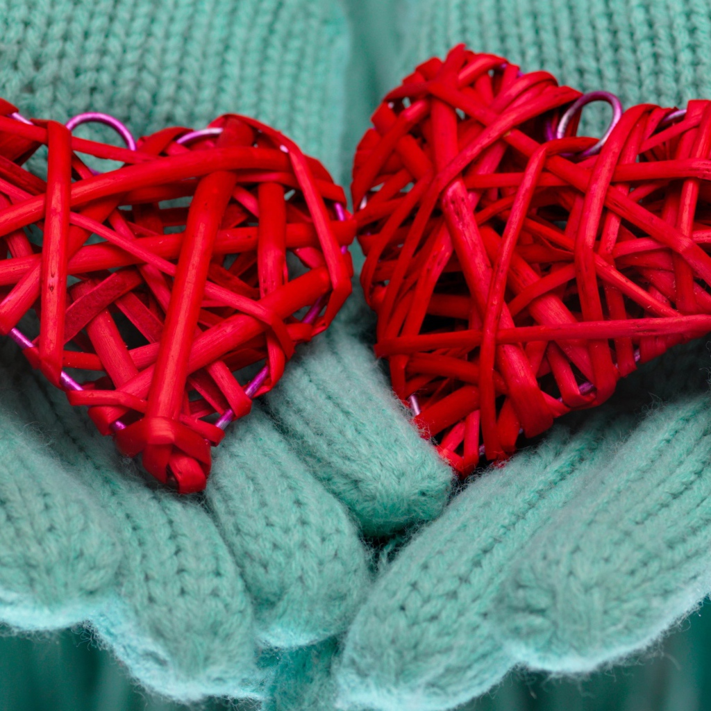 Два плетеных красных сердца лежать на руках в варежках