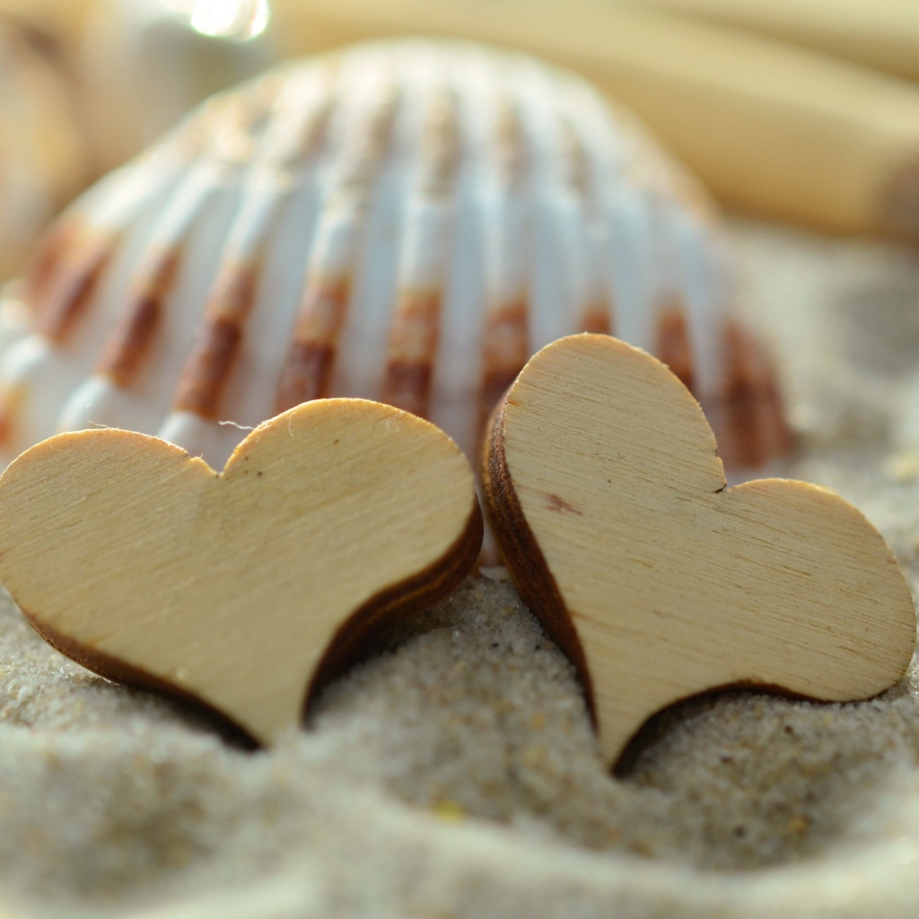 Два деревянных сердца и ракушки лежат на песке