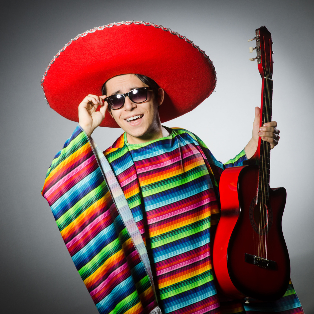 Мужчина в красном сомбреро с гитарой в руках на сером фоне