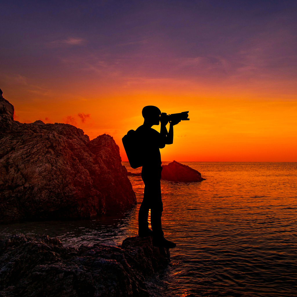 Мужчина фотографирует закат на берегу моря
