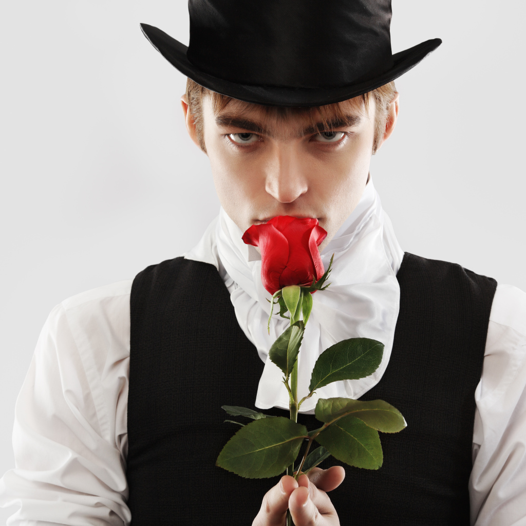 Парень в цилиндре с красной розой в руке на сером фоне