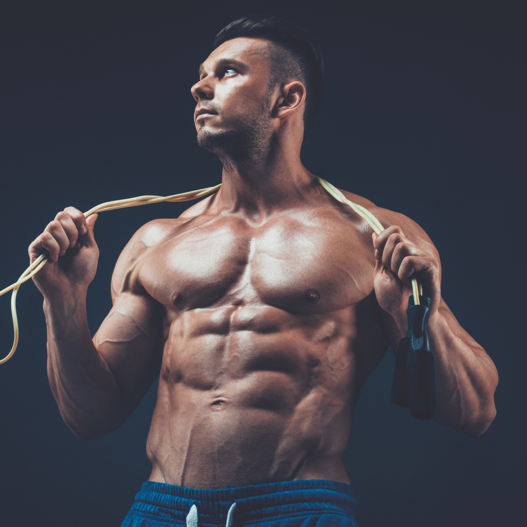 Накаченный мужчина со скакалкой в руках на сером фоне