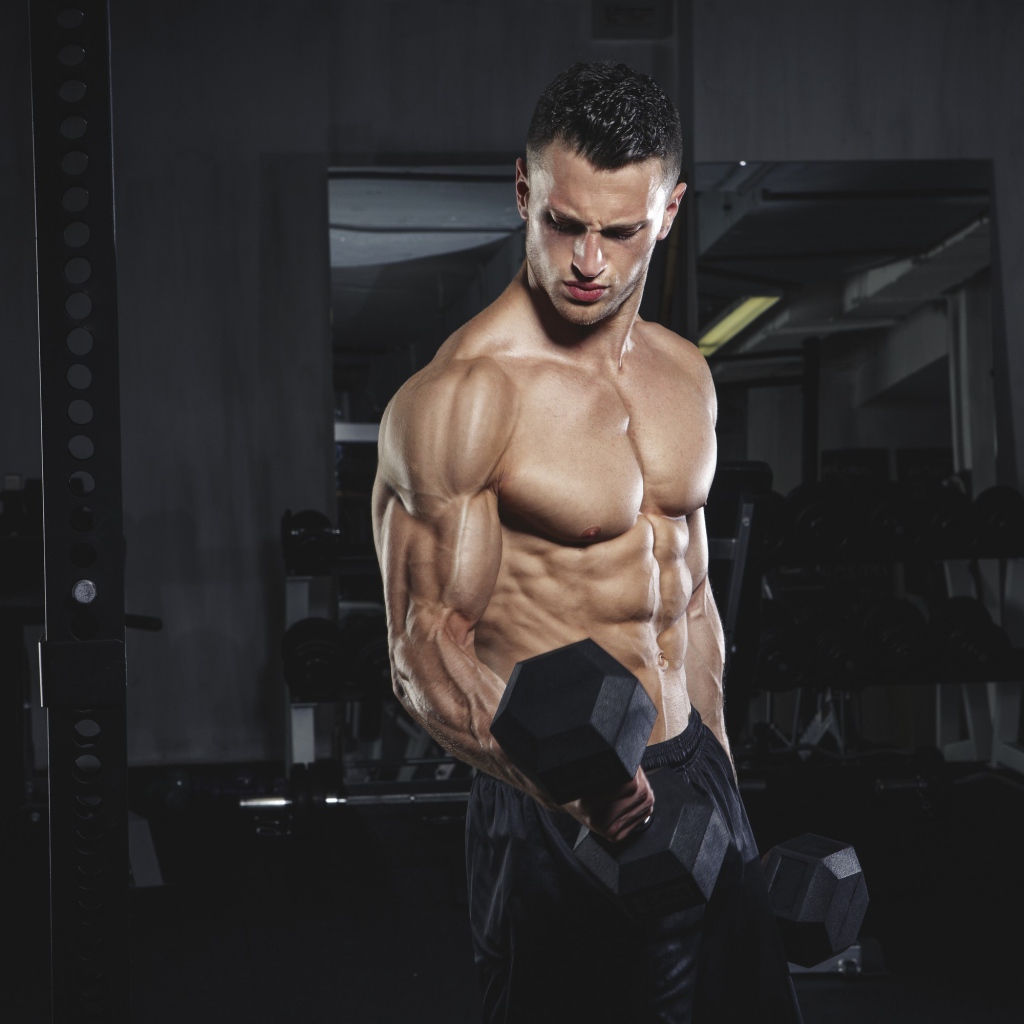 Накаченный мужчина с тяжелыми гантелями в руках 