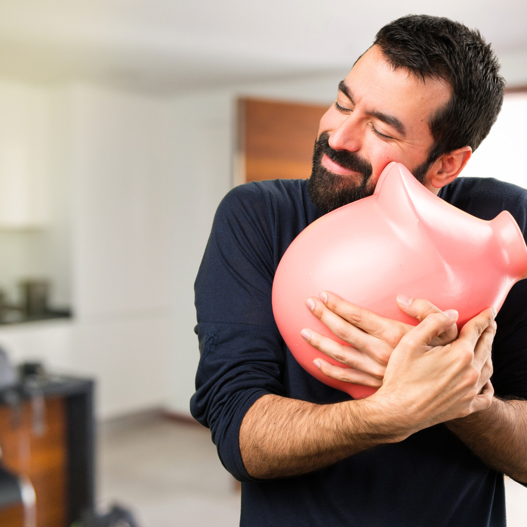 Мужчина обнимает розовую свинью копилку 