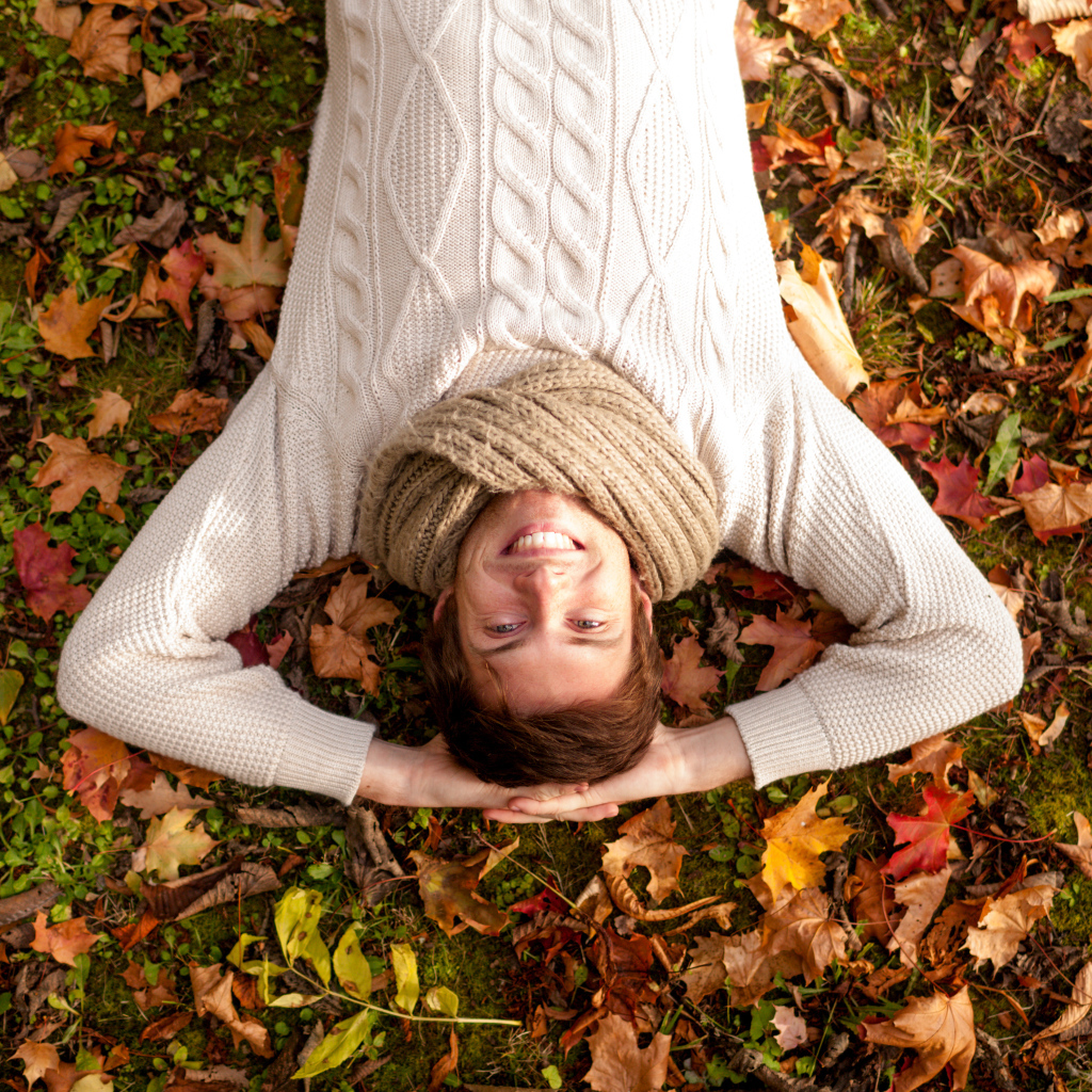 Улыбающийся мужчина в свитере лежит на опавших листьях 