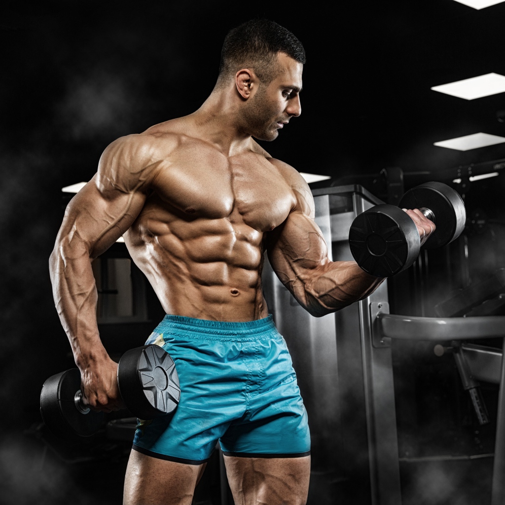 Сильный накаченный мужчина в шортах с гантелями в руках 