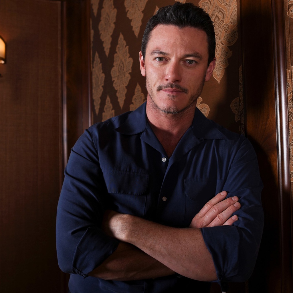 Актер Люк Эванс в рубашке стоит у стены