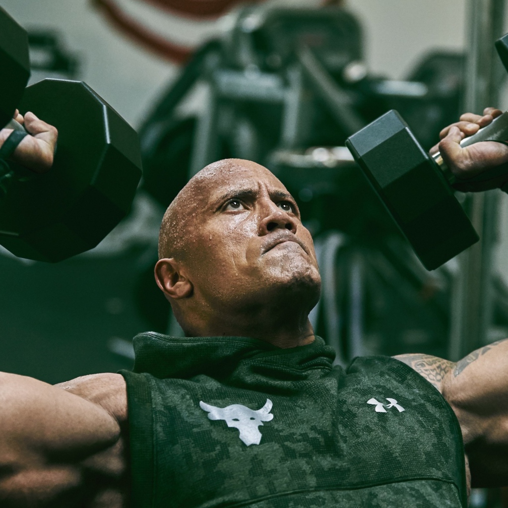 Американский актер, сильный мужчина Дуэйн Джонсон с гантелями в спортзале