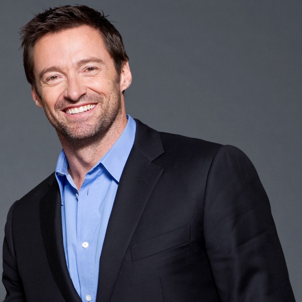 Улыбающийся мужчина, актер Хью Джекман  в костюме на сером фоне