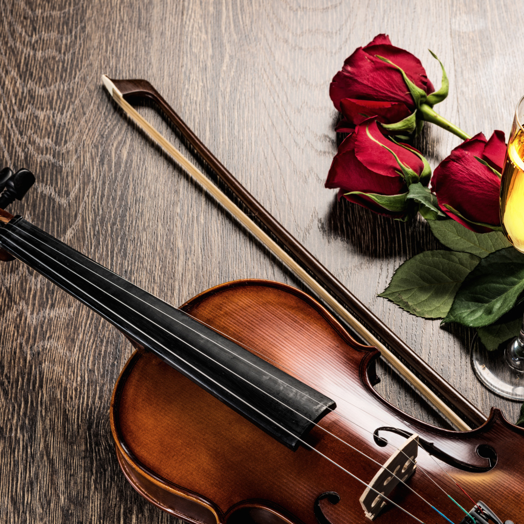 Скрипка лежит на столе с бокалом шампанского и красными розами