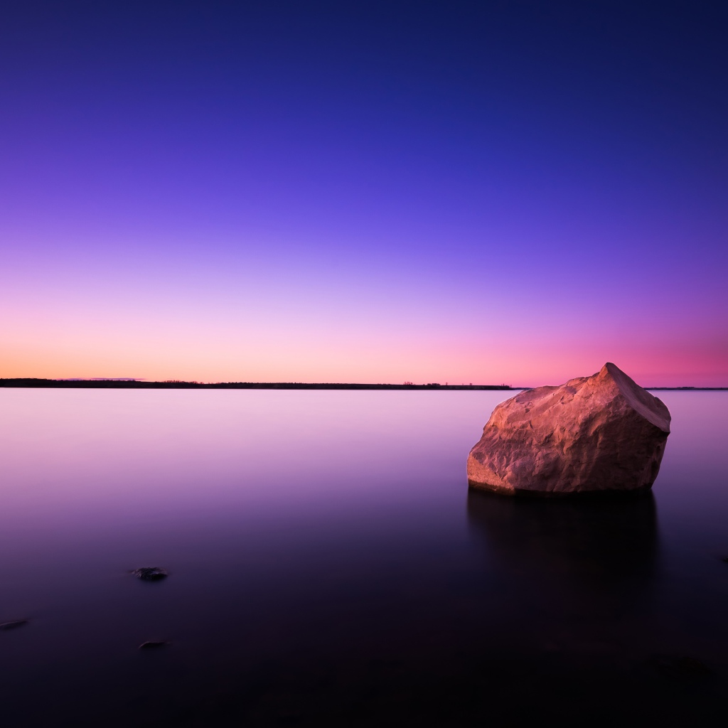 Большой камень в спокойной воде в сумерках
