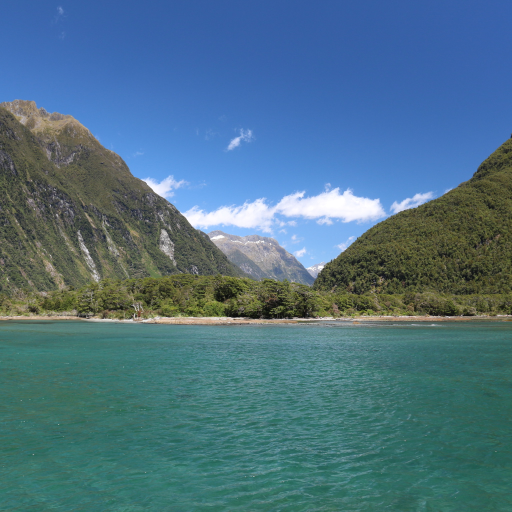 Голубая вода в озере на фоне покрытых зеленью гор под голубым небом