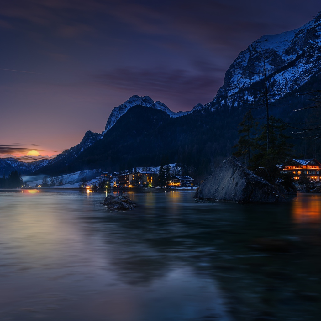 Город у озера на фоне заснеженных гор ночью 