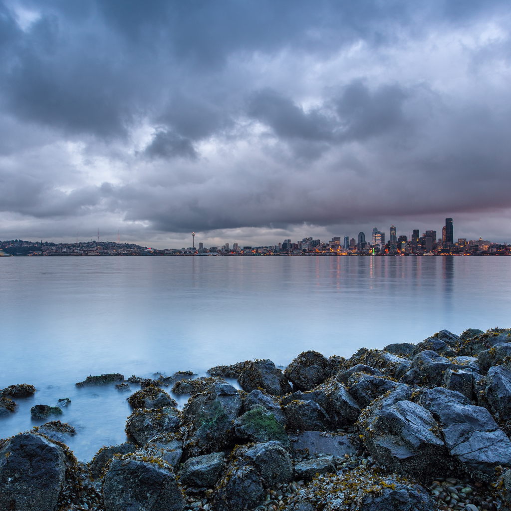 Камни на берегу реки на фоне города под пасмурным небом