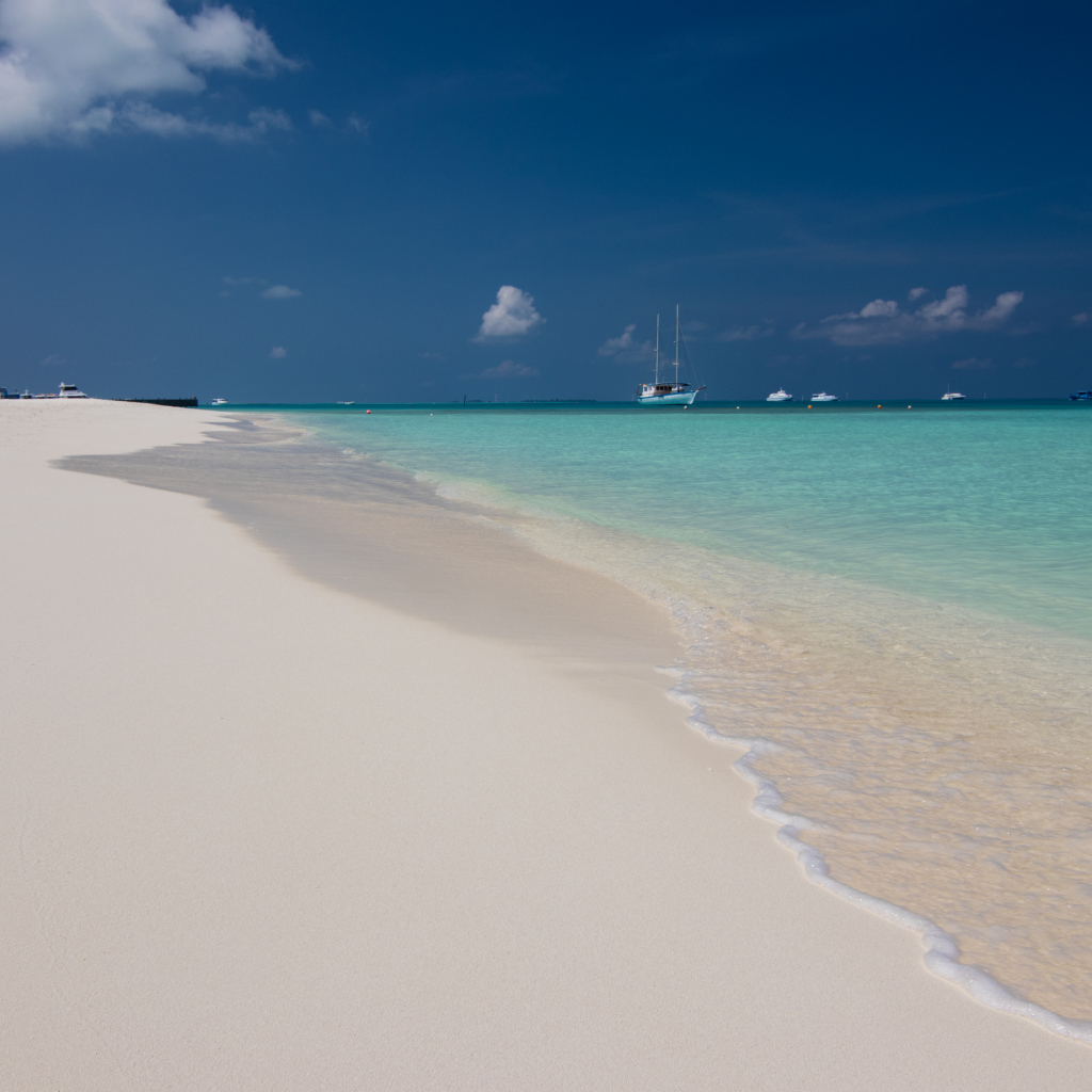 Спокойные волны на белом горячем песке под голубым небом
