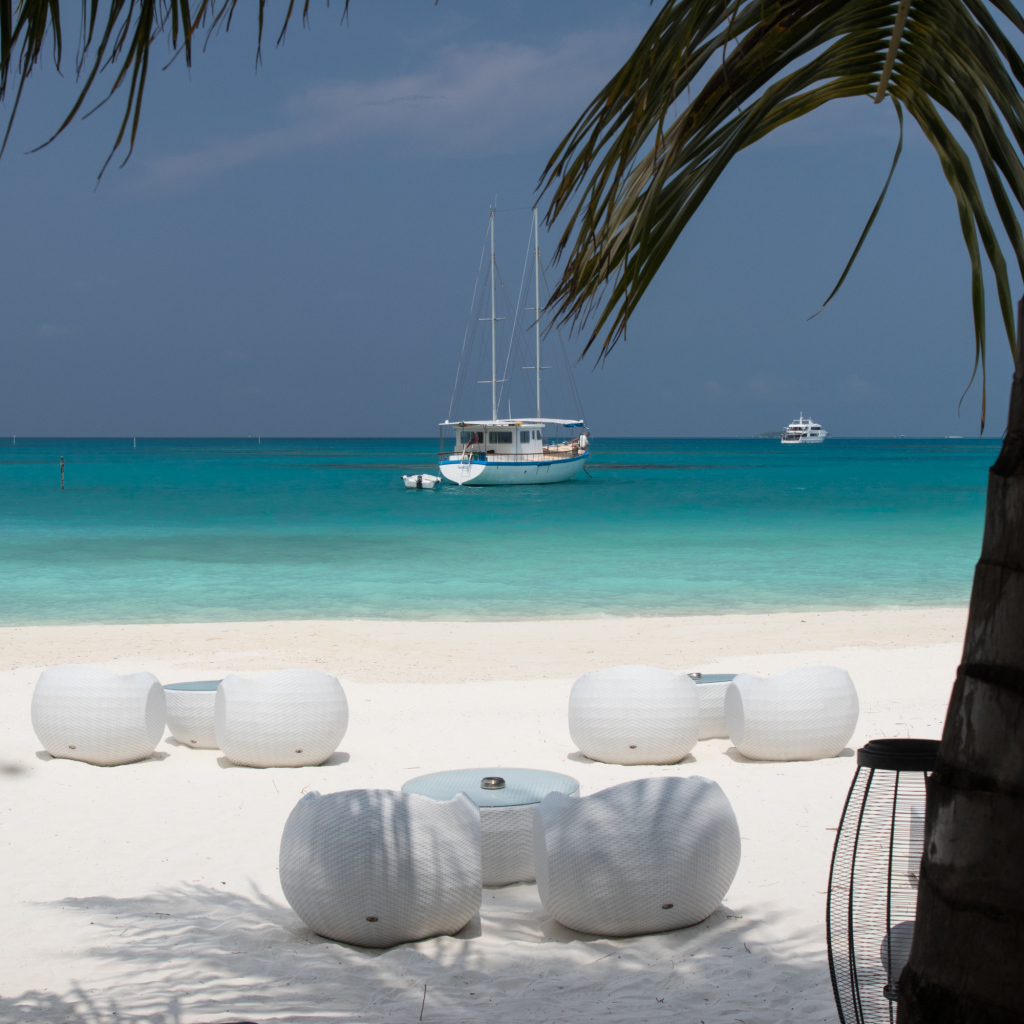 Белые кресла и столики на белом песке на пляже у голубой воды