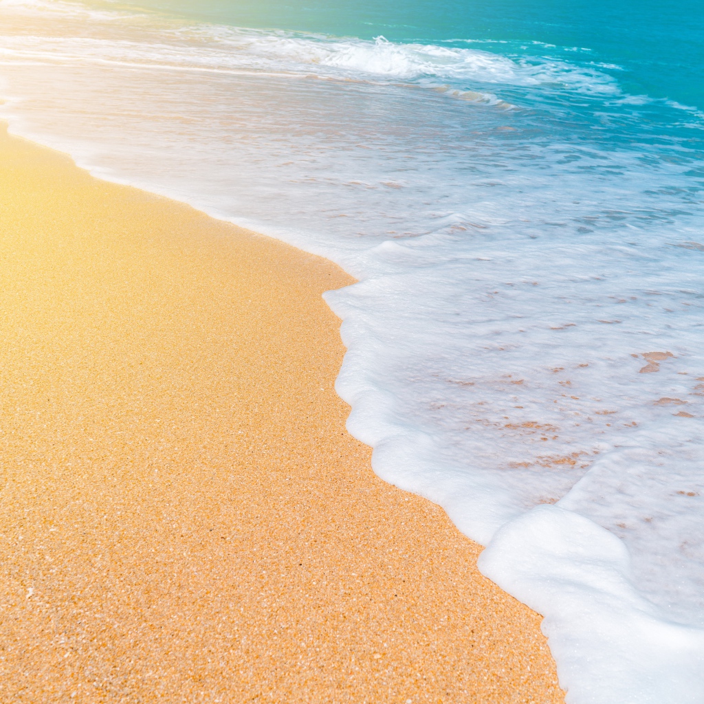 Белые волны океана омывают желтый горячий песок на пляже