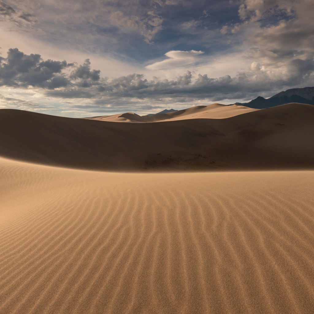 Волнистый песок под небом с белыми облаками