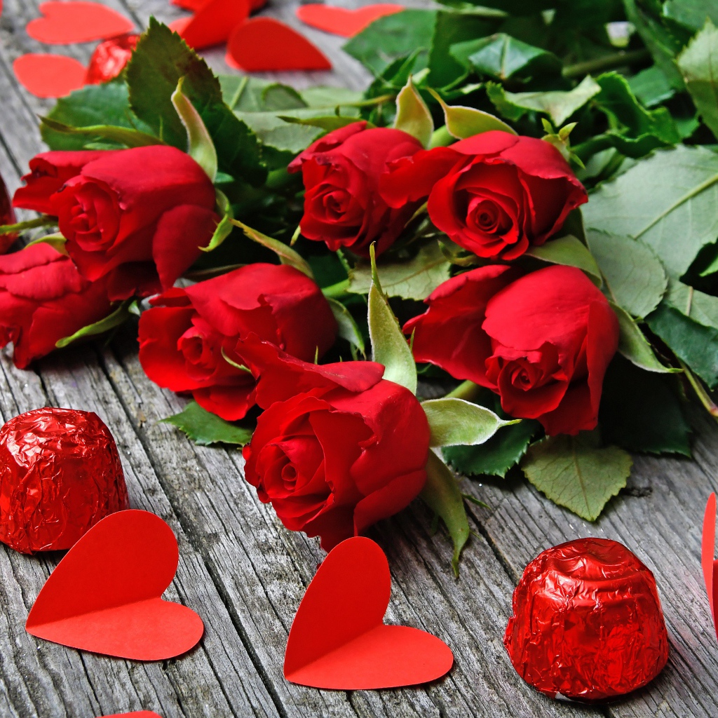Букет красных роз на деревянном столе с конфетами и красными сердечками