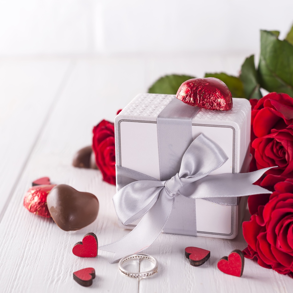 Подарок на столе с конфетами и букетом красных роз 