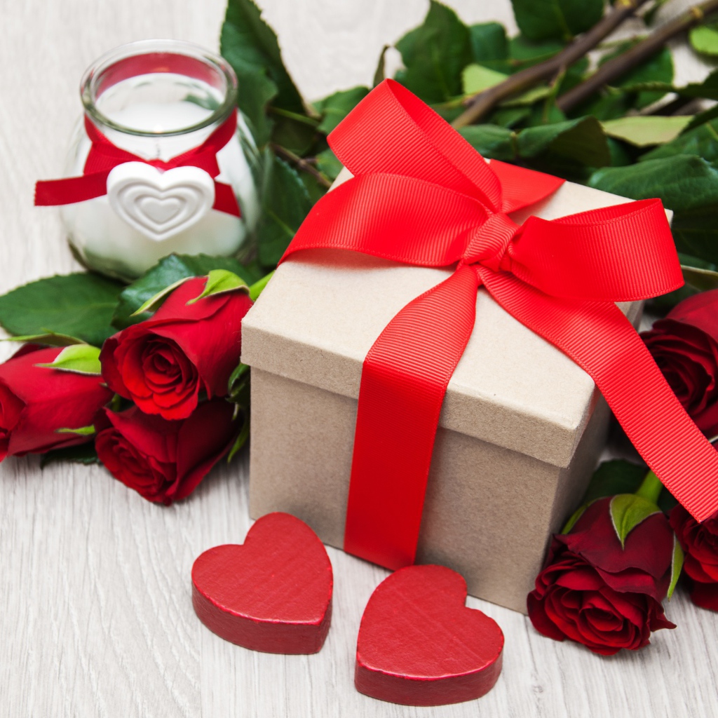 Красивый букет красных роз на столе со свечой и подарком