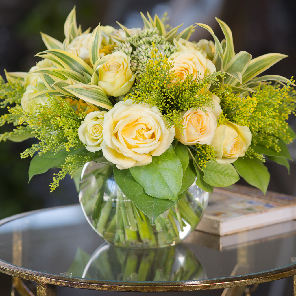 Красивый букет роз с зелеными листьями в в вазе на стеклянном столе