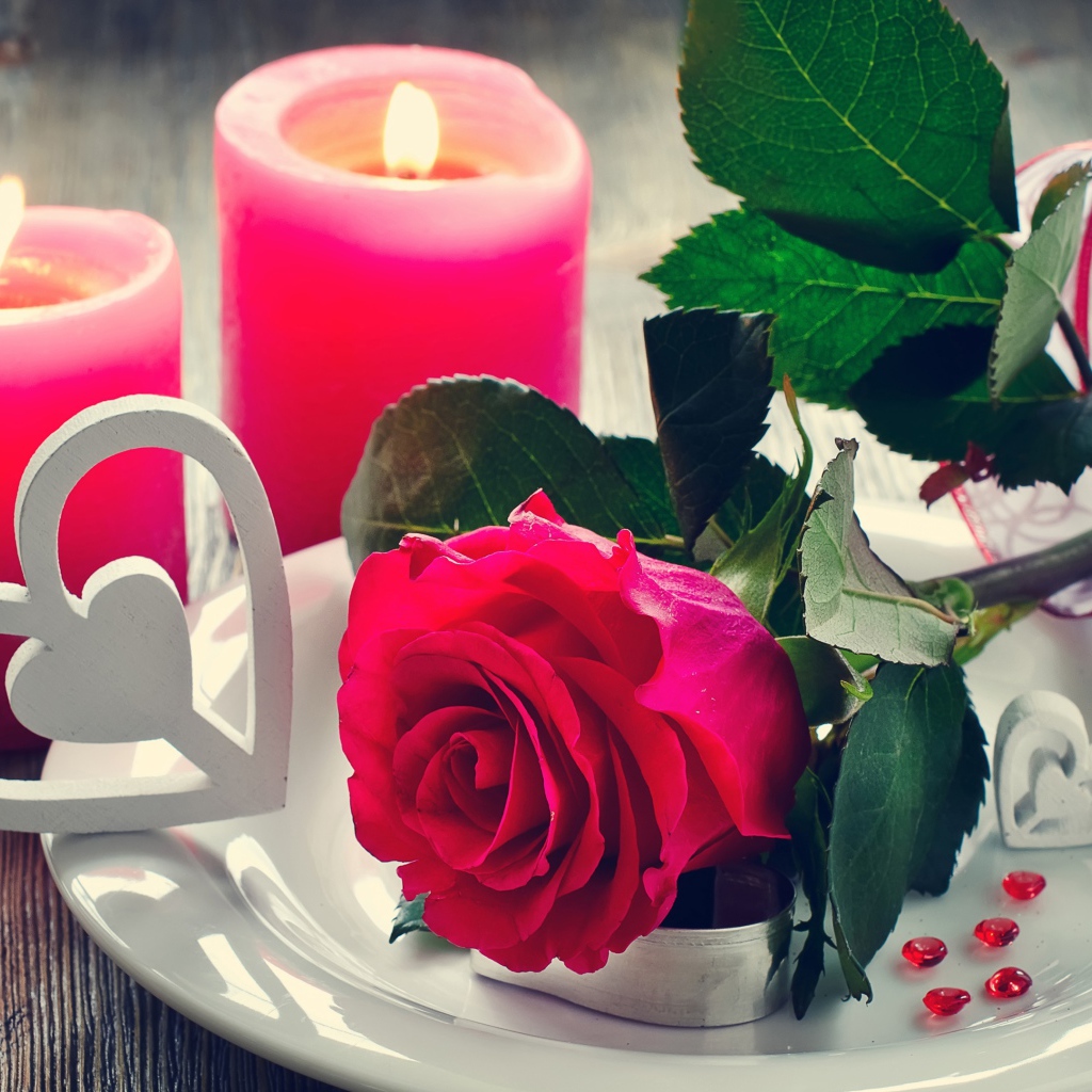 Красная роза на белой тарелке с сердечками на столе с зажженными свечами