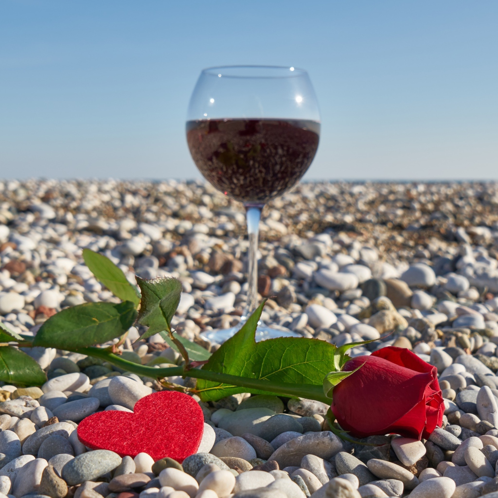 Красная роза на морской гальке с сердечком и бокалом вина