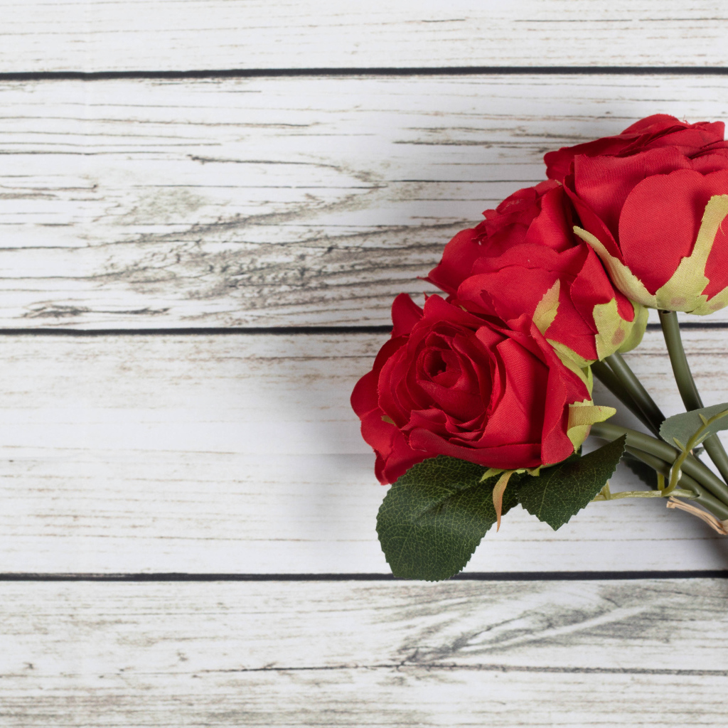Три искусственные красные розы на деревянном фоне