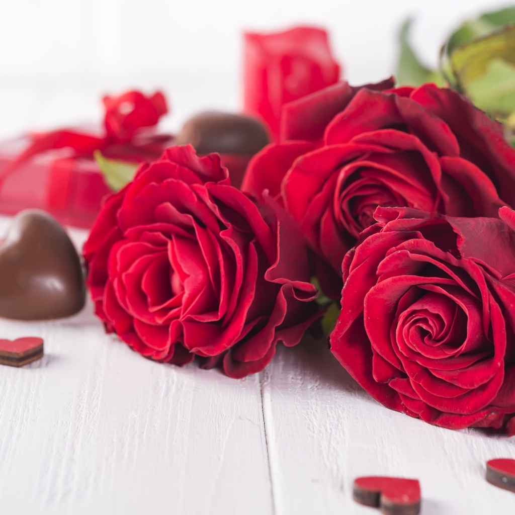 Три красивые красные розы на столе с конфетами