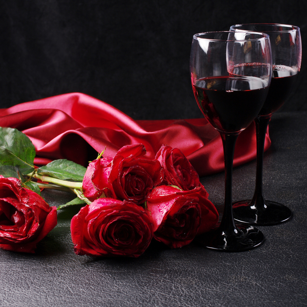 Два бокала с красным вином на черном фоне с букетом красных роз