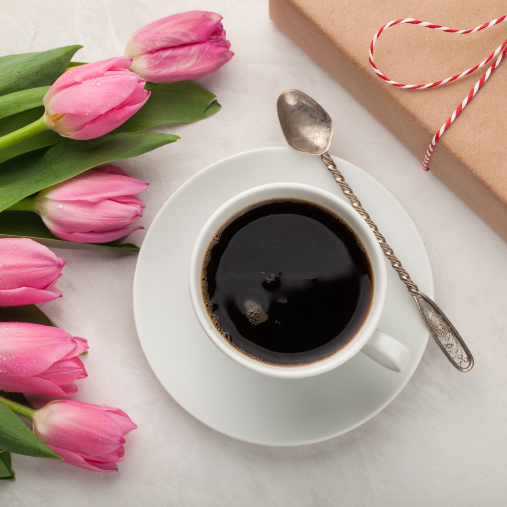 Белая чашка кофе на столе букетом розовых тюльпанов и подарком