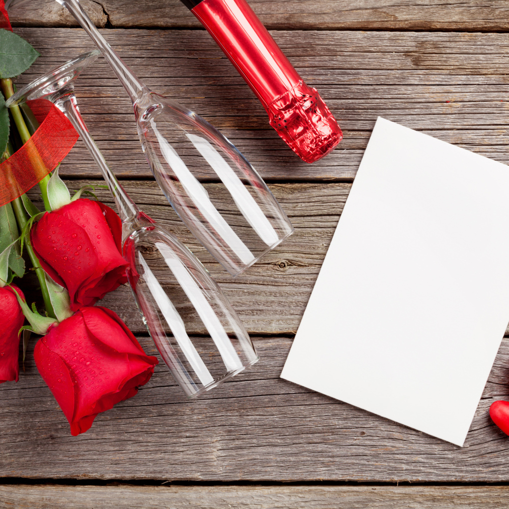 Белый лист бумаги на деревянном столе с бокалами и красными розами