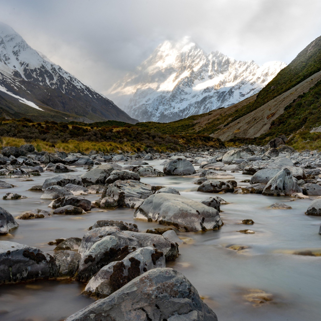 Камни в воде у заснеженных гор 