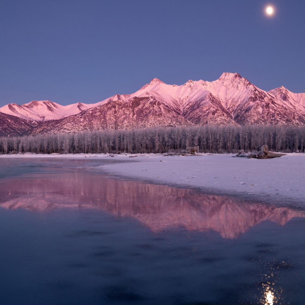 Луна над заснеженными горами отражается в заледеневшем озере 