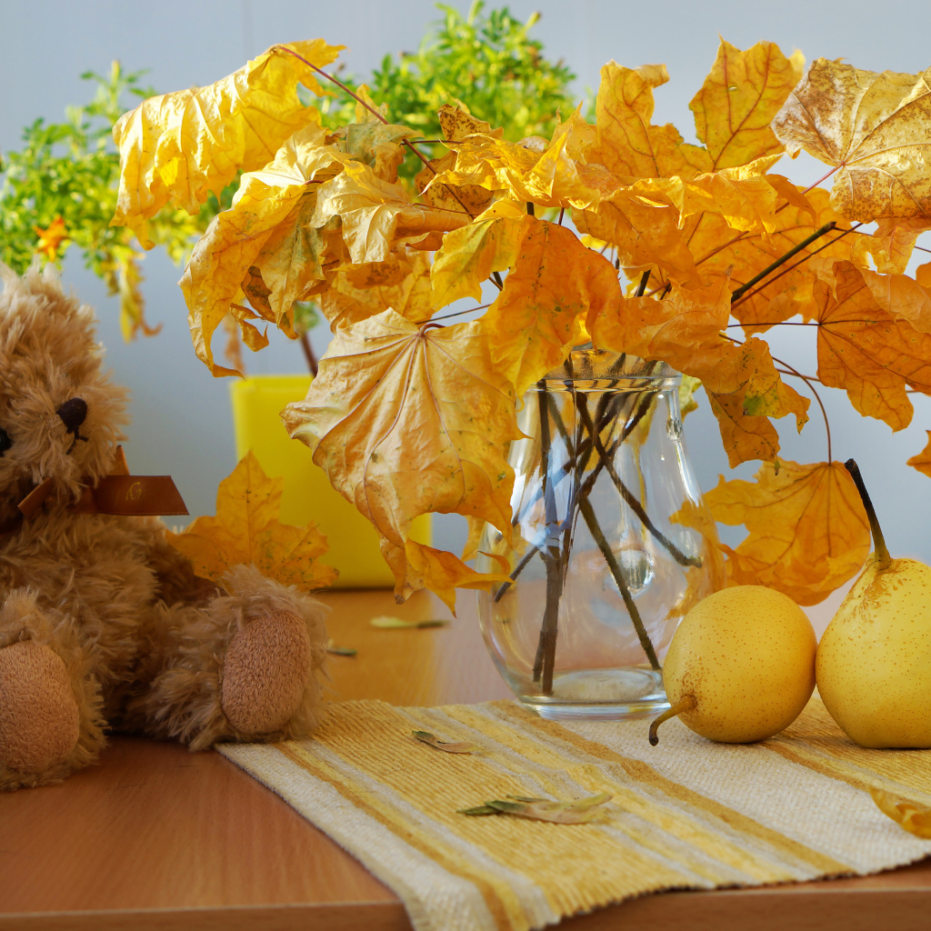 Игрушечный медведь на столе с желтыми осенними листьями и грушами
